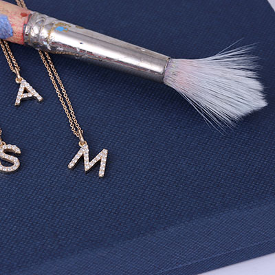 initial gold necklaces on textured fabric with brush